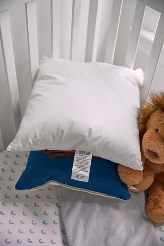 The crib setup includes a white pillow with a care tag and Sewing Down South 17 x 17 Indoor Nursery Inserts, placed on a blue one. A stuffed lion toy adds charm, while the mattress features a white sheet with colorful semi-circle patterns.