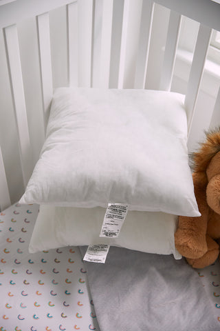 Stacked neatly in the crib, Sewing Down South 17 x 17 Indoor Nursery Inserts, filled with premium non-allergenic fiber for ultimate comfort, sit beside the bars. A plush toy peeks out on the right as a colorful sheet with small rainbows covers the mattress.