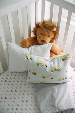 A stuffed lion sits in a white crib, surrounded by Sewing Down South 13 x 17 Indoor Nursery Inserts—one purely white and the other decorated with cheerful yellow school buses, while the mattress showcases colorful rainbows.